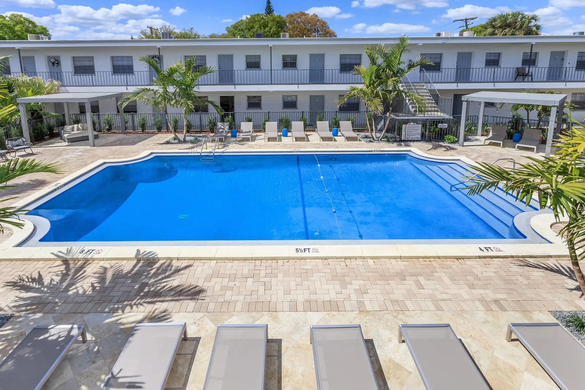 Luxury resort-style pool with lap lanes surrounded by contemporary white buildings, lounge chairs, and palm trees in St Petersburg residential community.