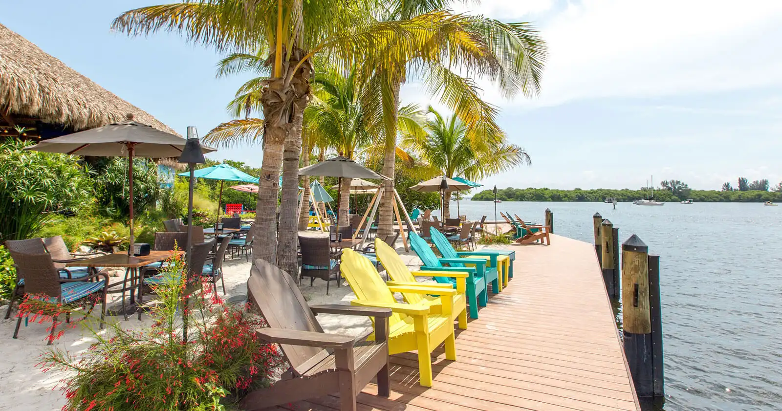 Luxury waterfront deck with yellow and turquoise Adirondack chairs, palm trees, and covered seating areas overlooking calm water in St Petersburg, FL.