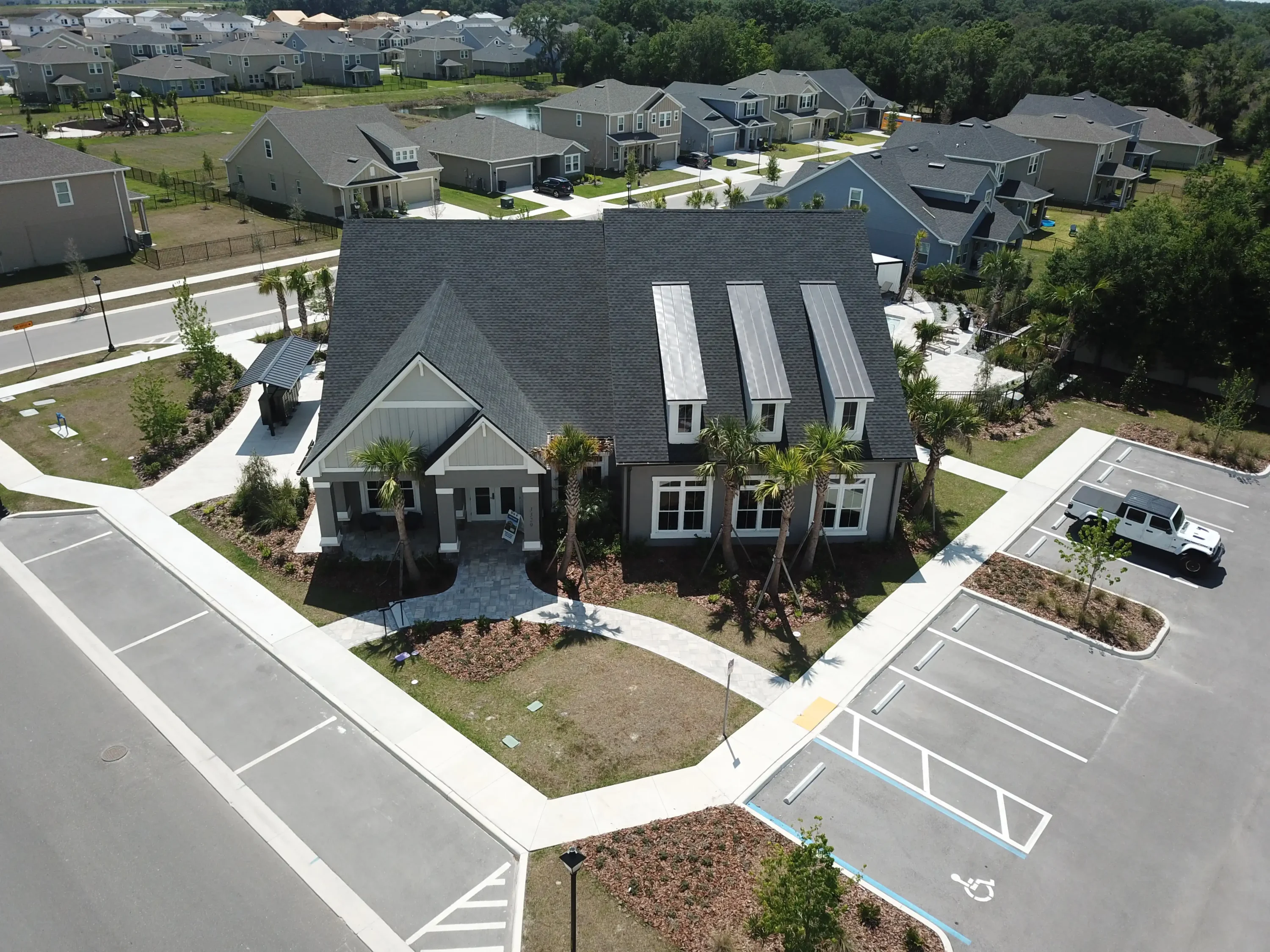 Aerial view of gray colonial-style home with three solar panels on roof, palm trees, and white driveway in St Petersburg residential community