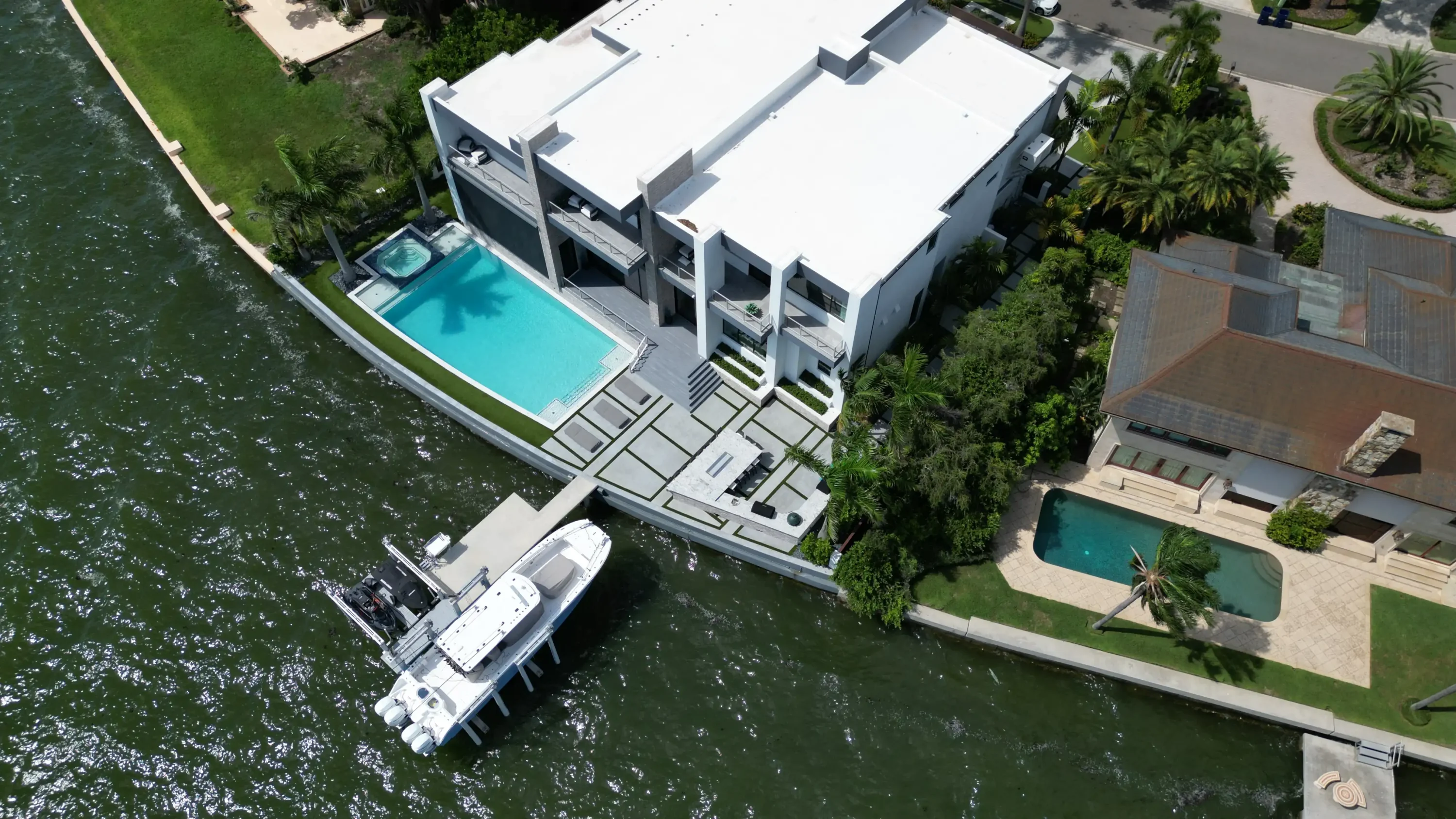 Aerial view of contemporary St. Petersburg luxury home with turquoise pool, white roof, private dock, and manicured waterfront landscape.