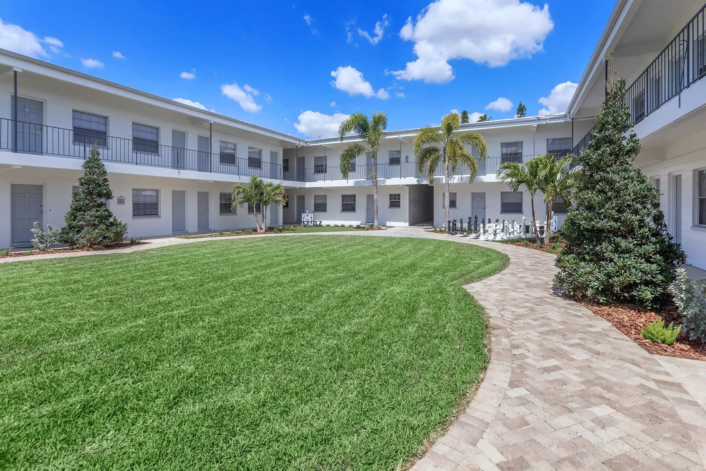 Luxury residential community courtyard with manicured lawn, white multi-story buildings, palm trees, and brick walkways in St Petersburg.