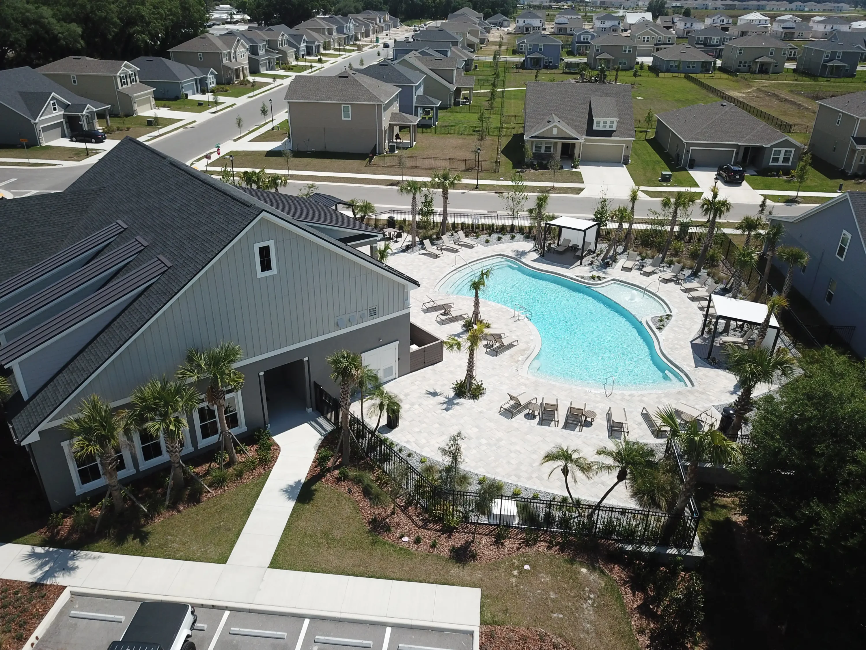Aerial view of curved resort pool with lounge seating, surrounded by modern homes in St Petersburg residential community with luxury landscape design.