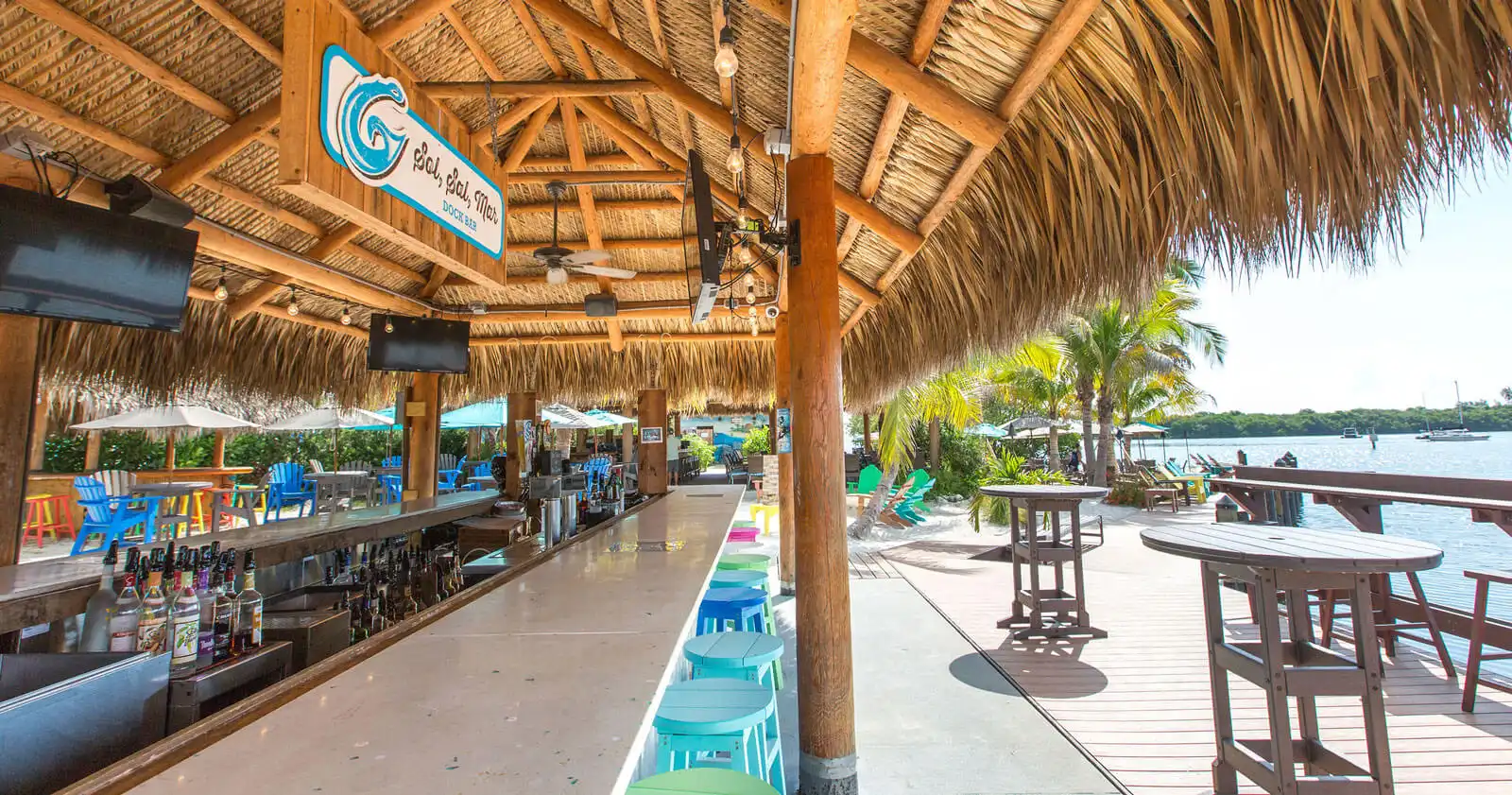 Luxury waterfront bar with thatched roof, blue seating, and wooden deck overlooking water in St Petersburg, FL.