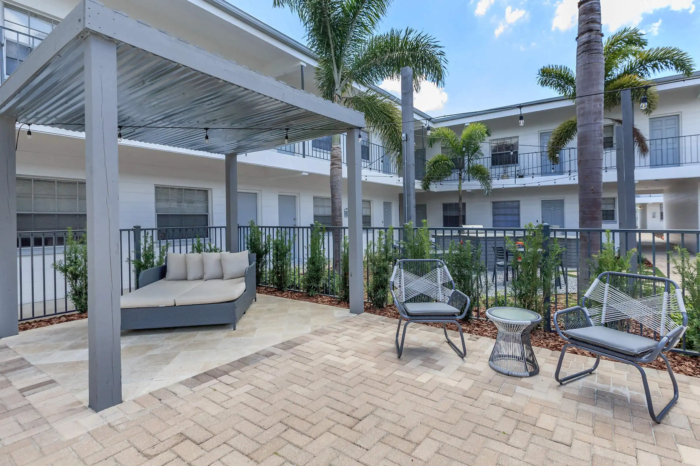 Contemporary courtyard with louvered pergola, outdoor furniture, and white residential buildings surrounding a paved patio in St Petersburg.