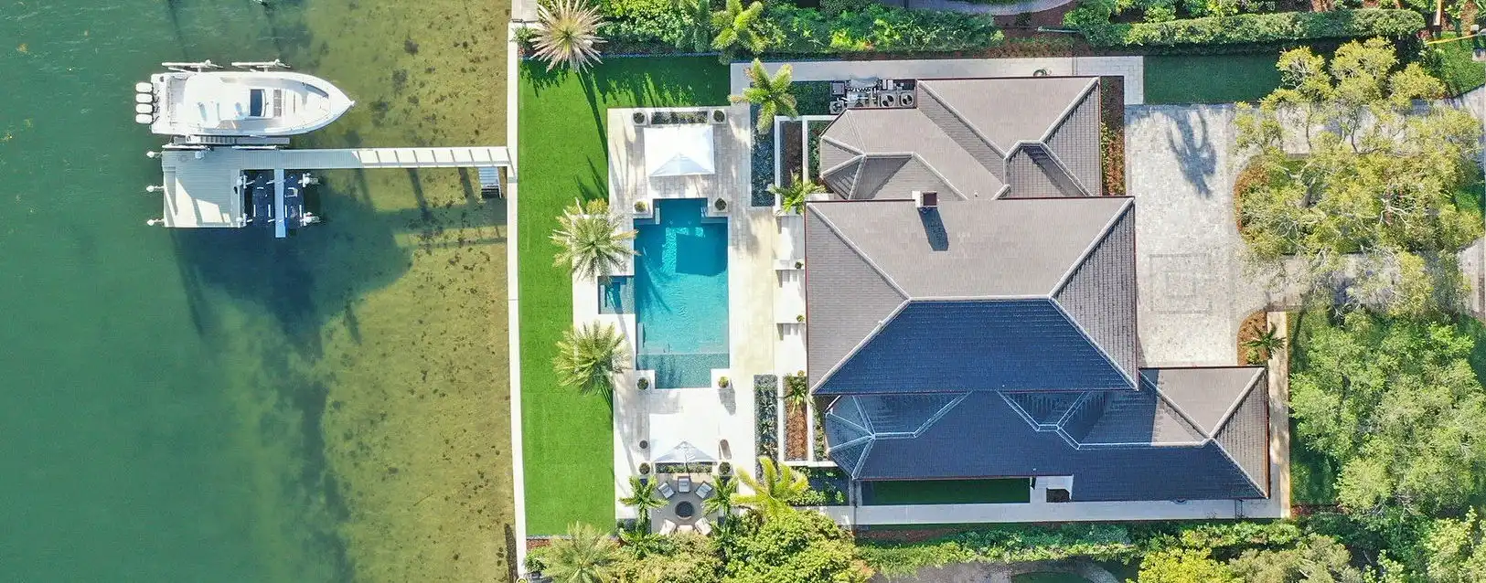 Aerial view of luxury waterfront home with dark blue roof, resort-style pool, and private boat dock on St Petersburg waterway.