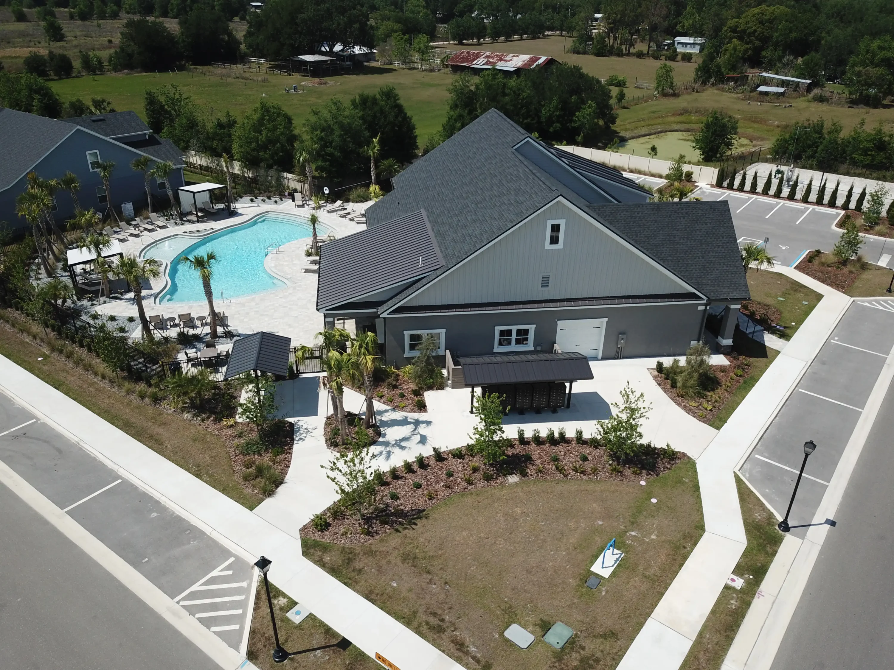 Aerial view of contemporary gray home with charcoal metal roof beside curved resort-style pool and manicured landscape in St Petersburg residential community.