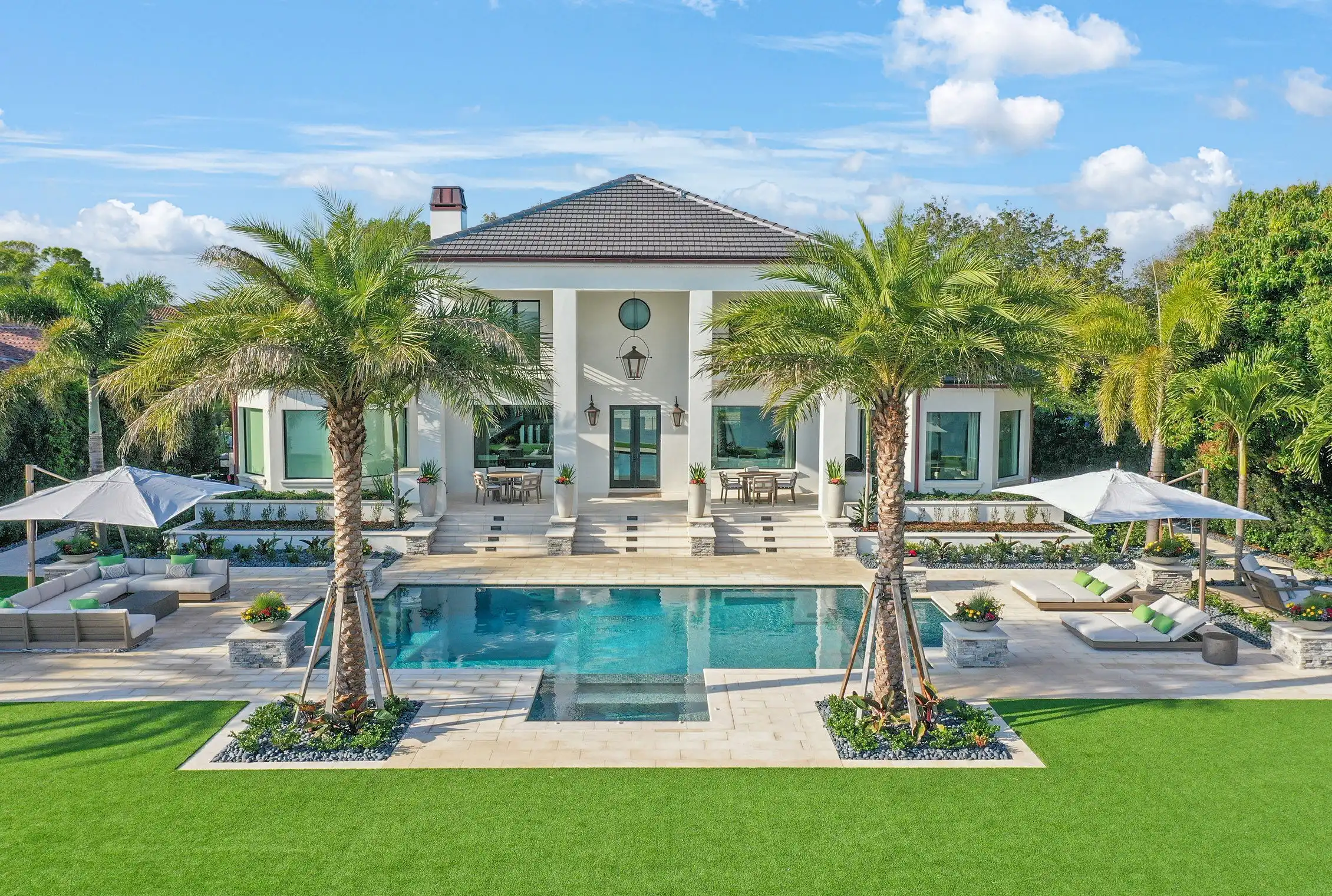 Modern white stucco home with dark hip roof and turquoise swimming pool, flanked by palm trees in luxury St Petersburg residential setting.