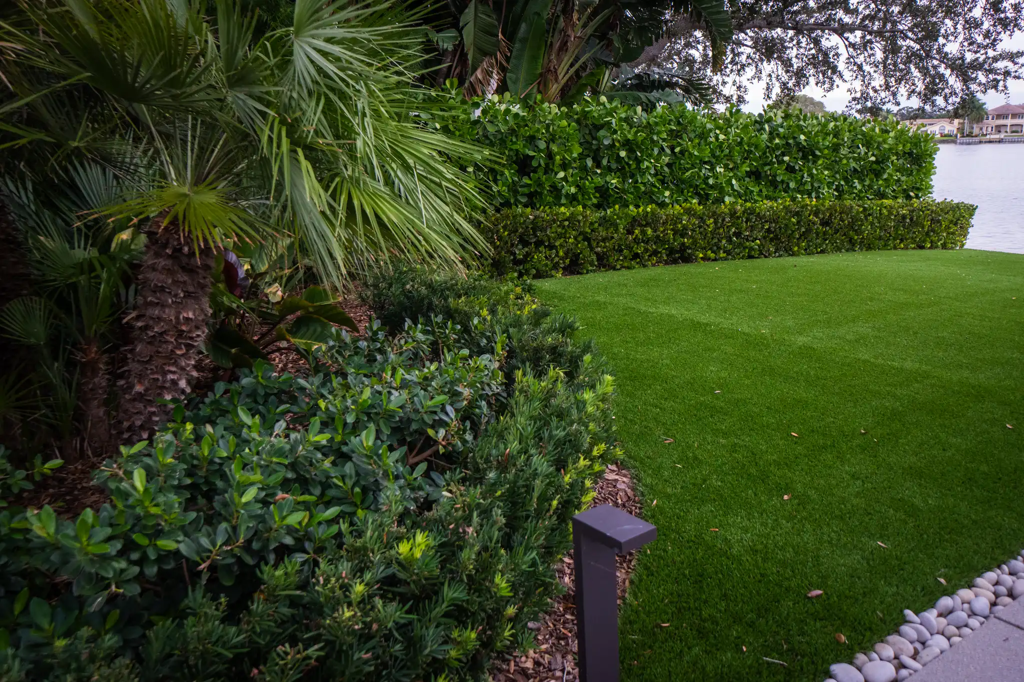 Manicured lawn with palm trees and sculpted hedges bordering a waterfront property in St Petersburg, FL luxury residential landscape design.