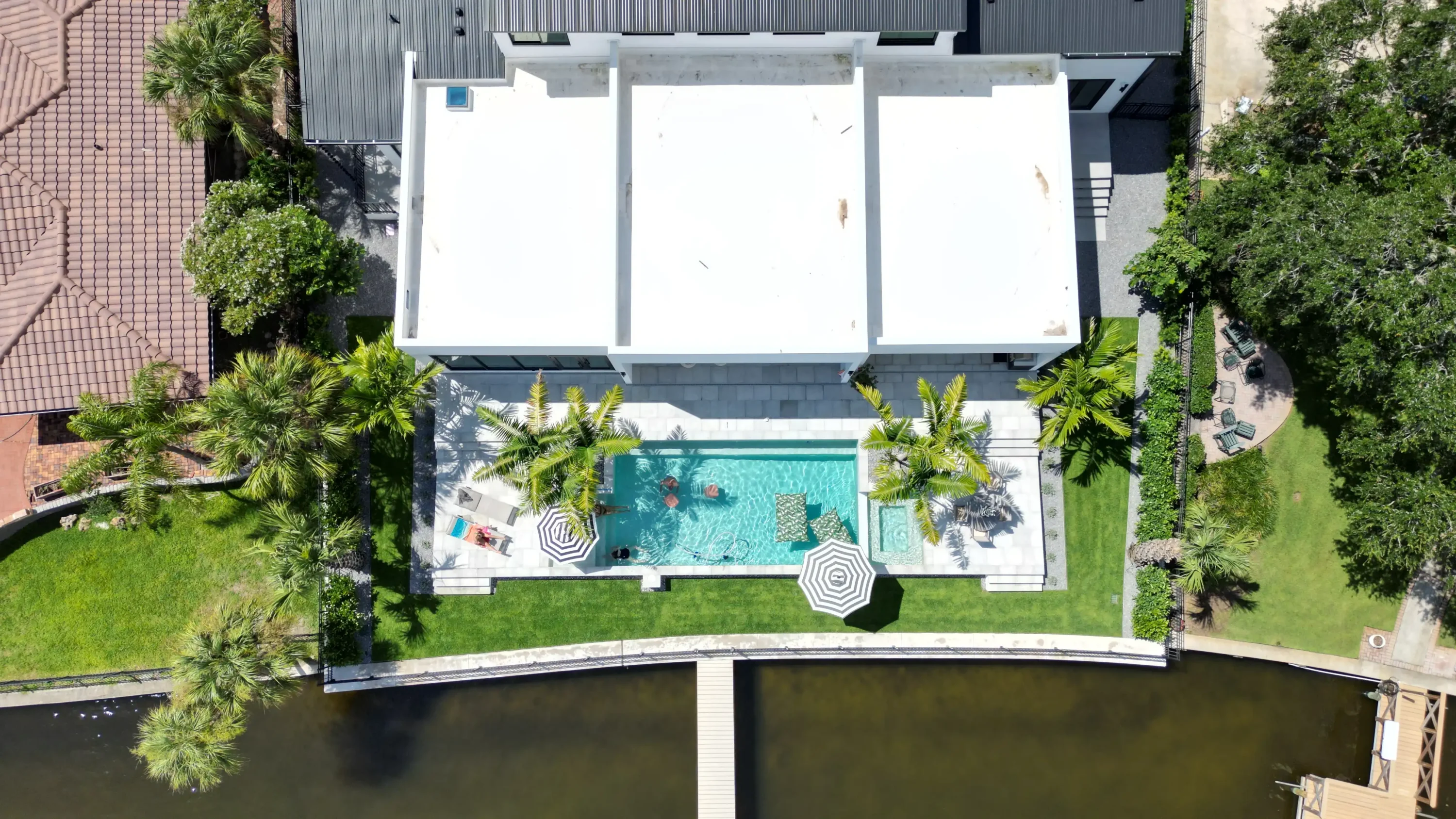 Aerial view of contemporary waterfront home with turquoise pool, manicured lawn, and tropical landscaping in St Petersburg, FL.