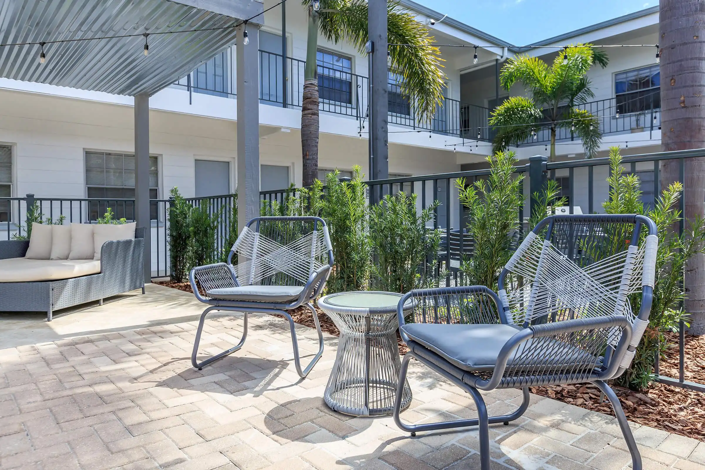 Modern luxury outdoor courtyard with gray woven chairs, potted plants, and multi-story residential architecture in St Petersburg, FL featuring sophisticated landscape design.