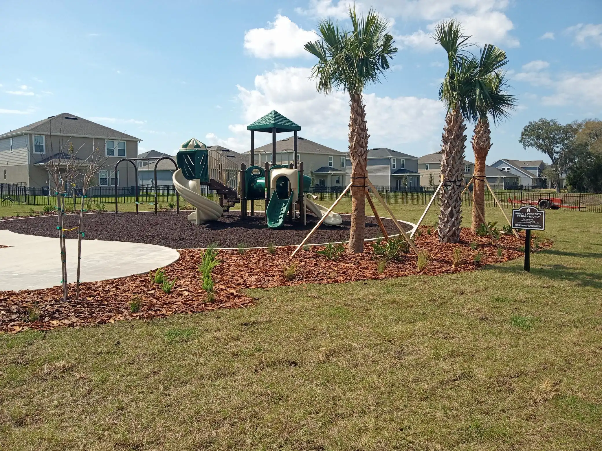 Modern playground with green slide tower, palm trees, and residential homes in luxury St Petersburg community with manicured landscape design.