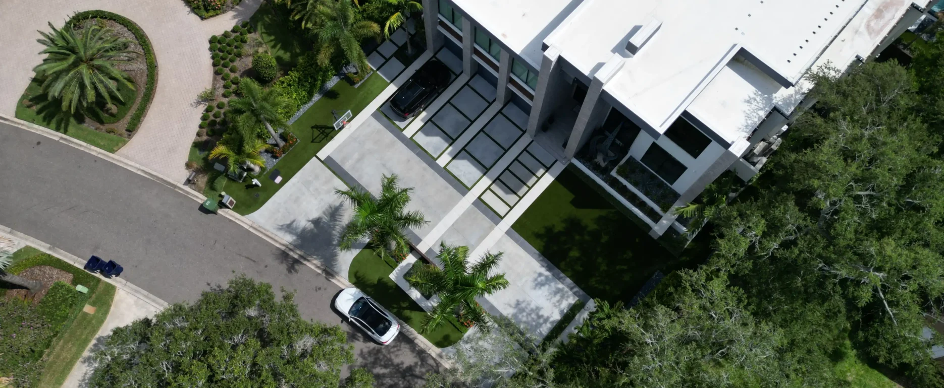 Aerial view of contemporary residential homes with white roofs, manicured lawns, palm trees, and driveway in St Petersburg luxury community.