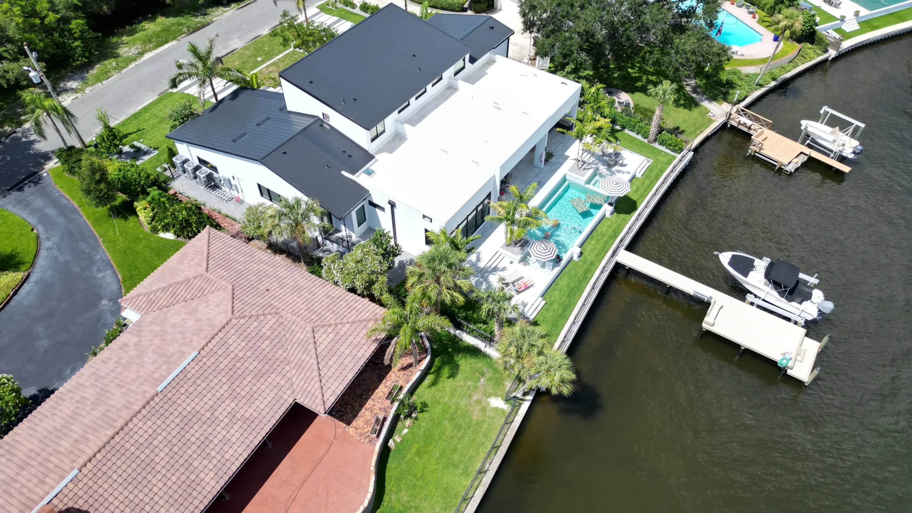 Aerial view of contemporary white home with pool, manicured lawn, and private boat dock on waterfront in St Petersburg, FL luxury residential community.