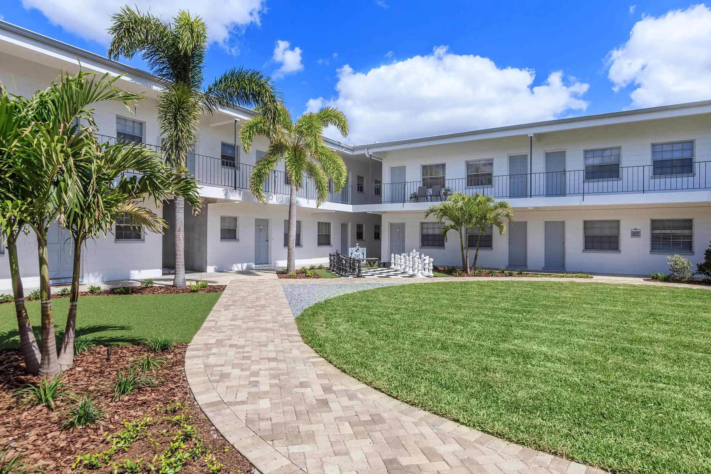 Modern white residential complex with manicured lawn, palm trees, and brick patio in St Petersburg luxury community development.