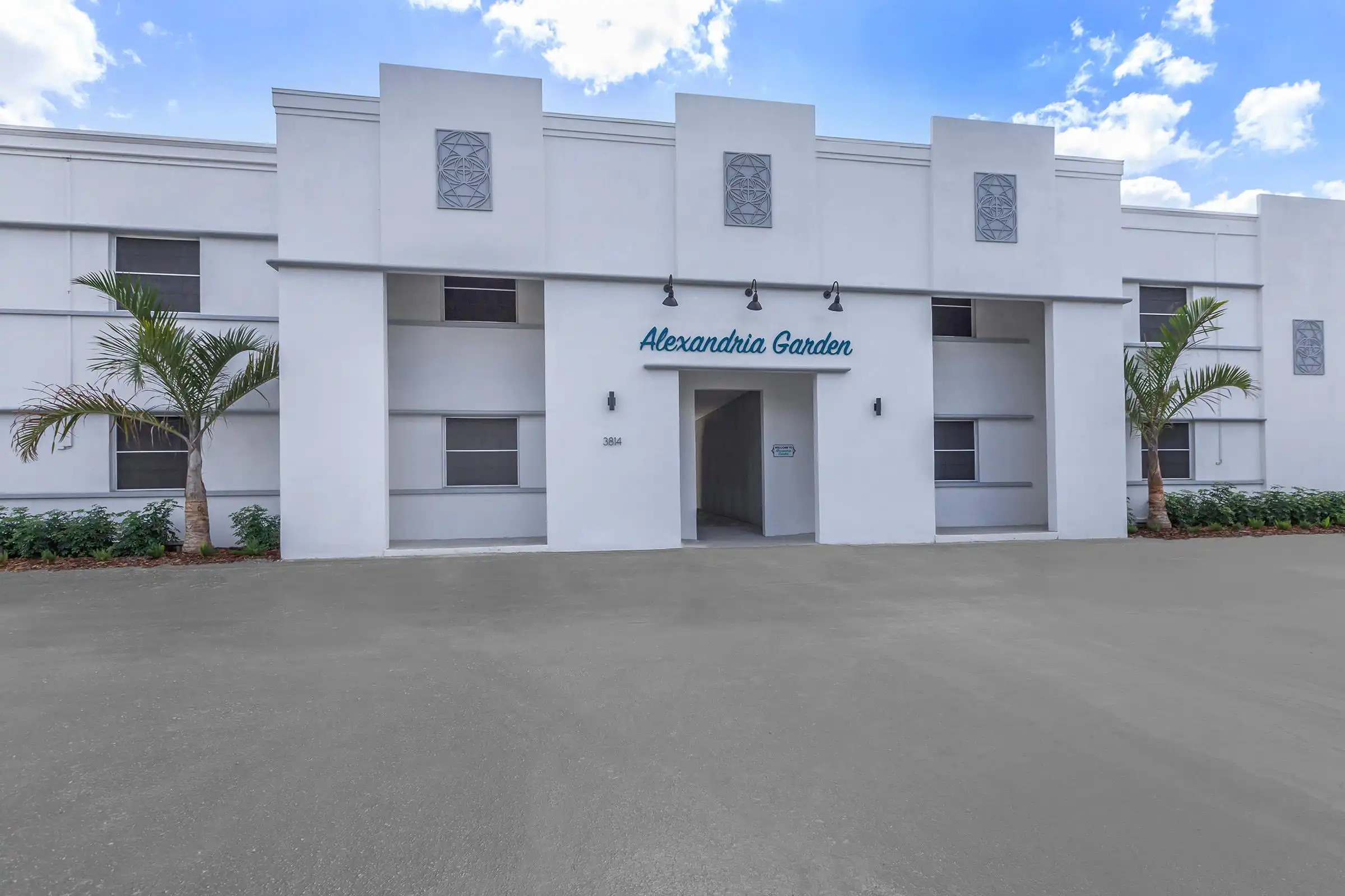Modern white Art Deco building facade with geometric details, palm trees, and Alexandria Garden signage in St Petersburg, FL residential community.