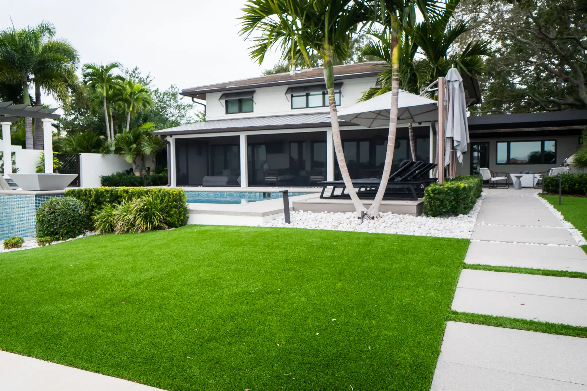 Contemporary white house with expansive pool deck, manicured lawn, and palm trees in luxury St Petersburg residential community.