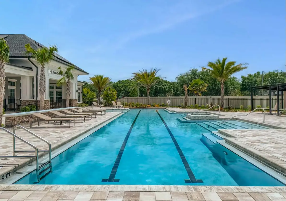 Resort-style lap pool with lane dividers, white modern clubhouse, palm trees, and lounge seating at luxury residential community in Florida.