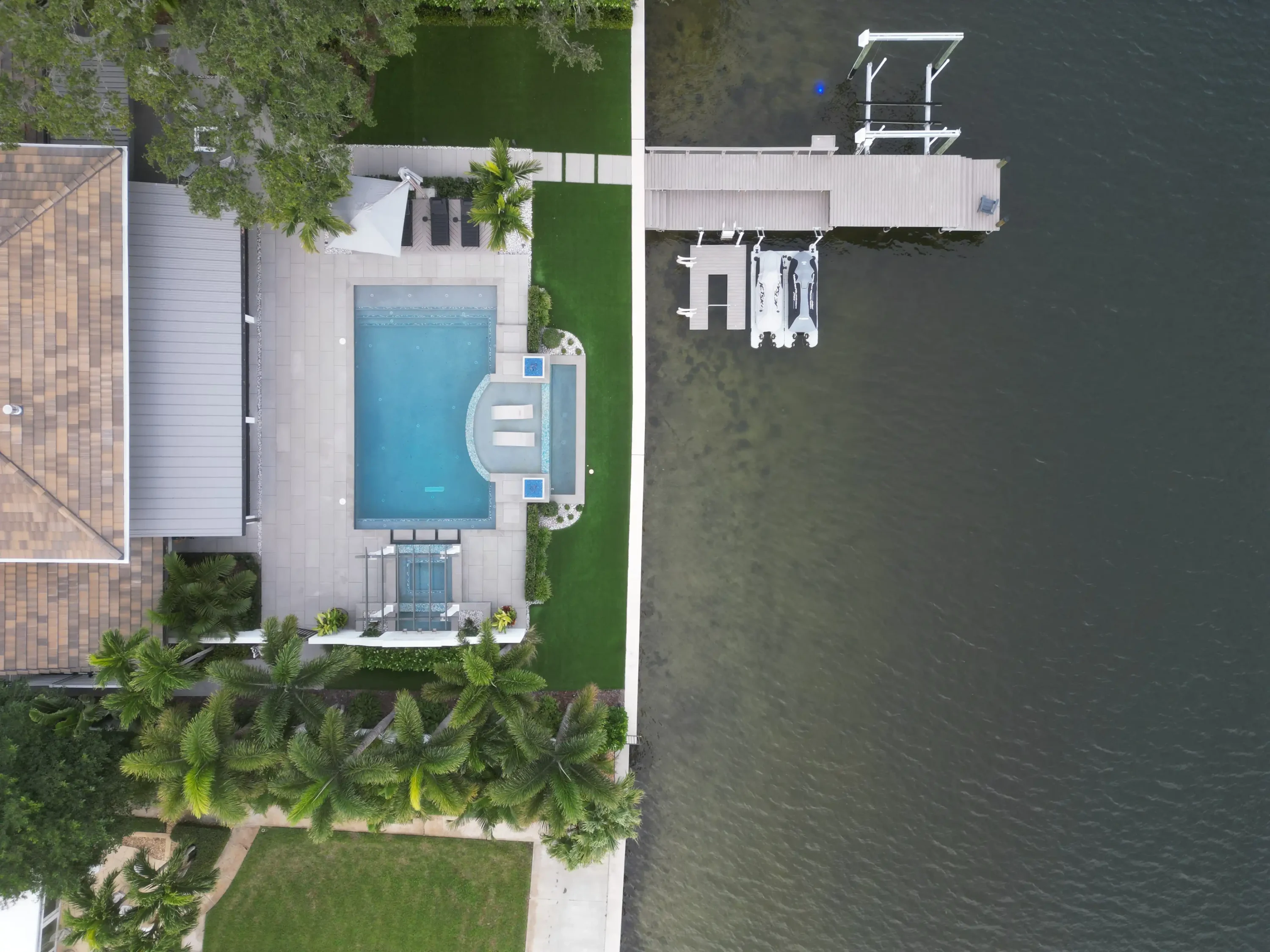 Aerial view of contemporary waterfront home featuring luxury pool design, manicured landscape, and private boat dock on calm water in St Petersburg, FL.