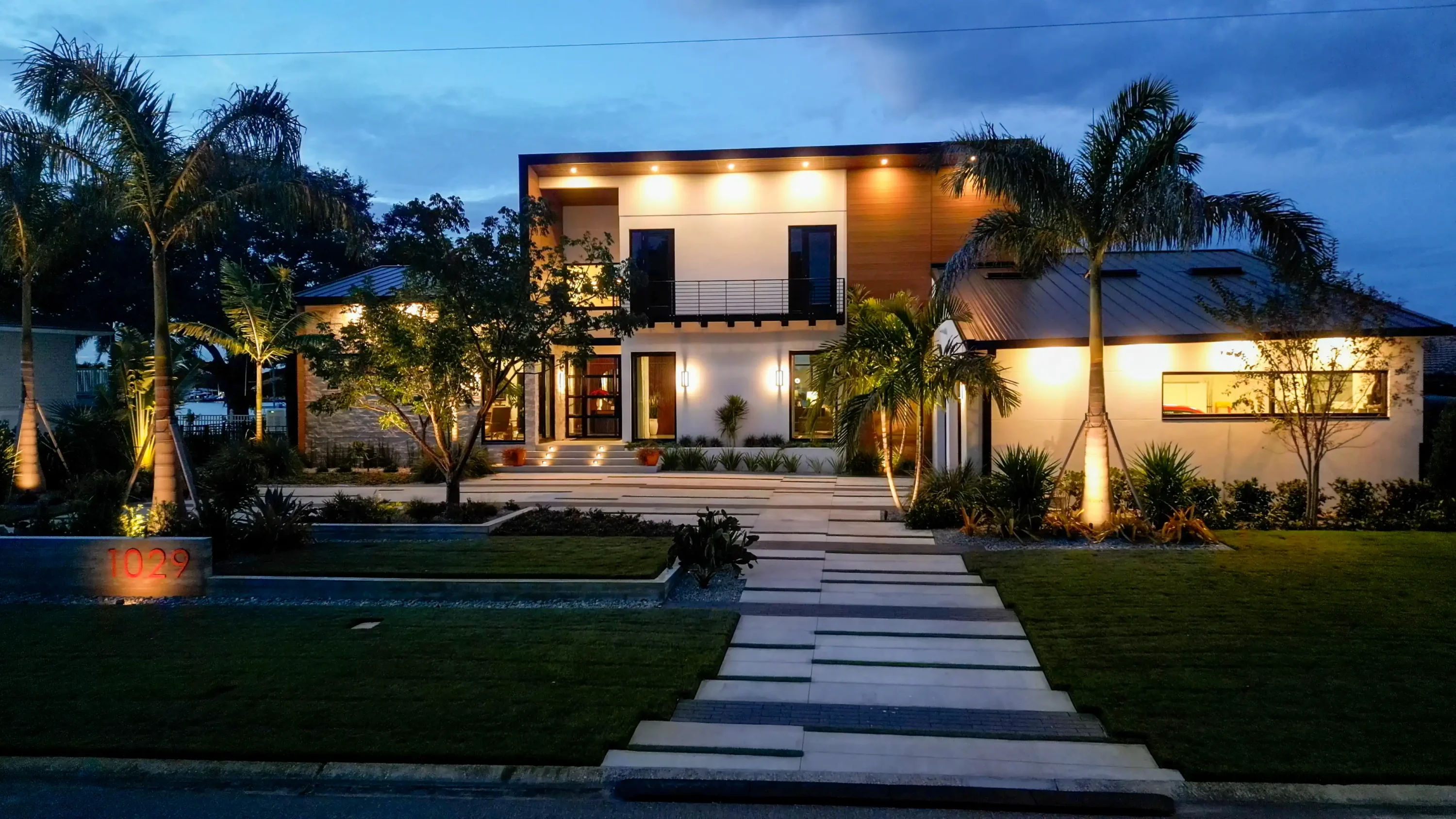 Contemporary white residence with warm landscape lighting, palm trees, and stone pathway in St Petersburg luxury residential community