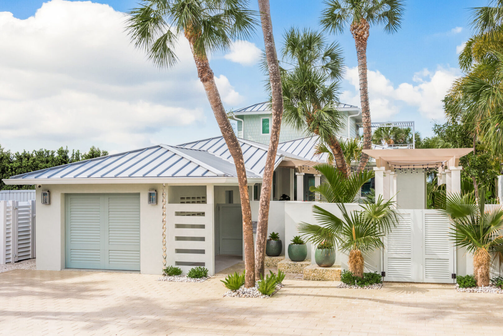 Contemporary white home with standing seam metal roof, surrounded by tall palm trees and white fence, showcasing luxury residential architecture in St Petersburg, Florida.