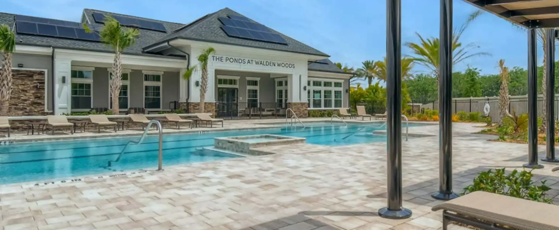 Luxury pool deck with blue swimming pool, modern white clubhouse, pergola seating area, and manicured landscape in St Petersburg residential community.