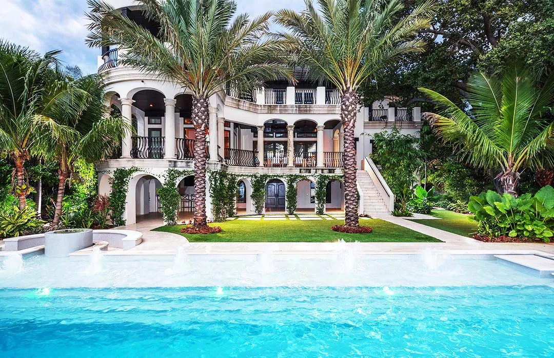 Luxury residential estate with white colonial architecture, crystal blue swimming pool, manicured lawn, and palm trees framing the property in St Petersburg, FL.