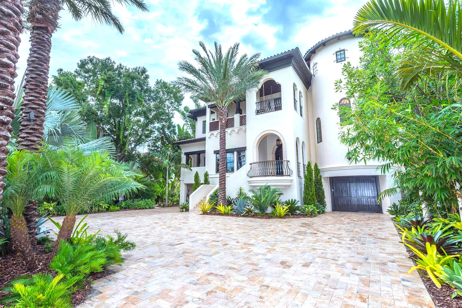 Luxury white Spanish colonial home with curved brick driveway, palm trees, and lush landscape design in St Petersburg, Florida.