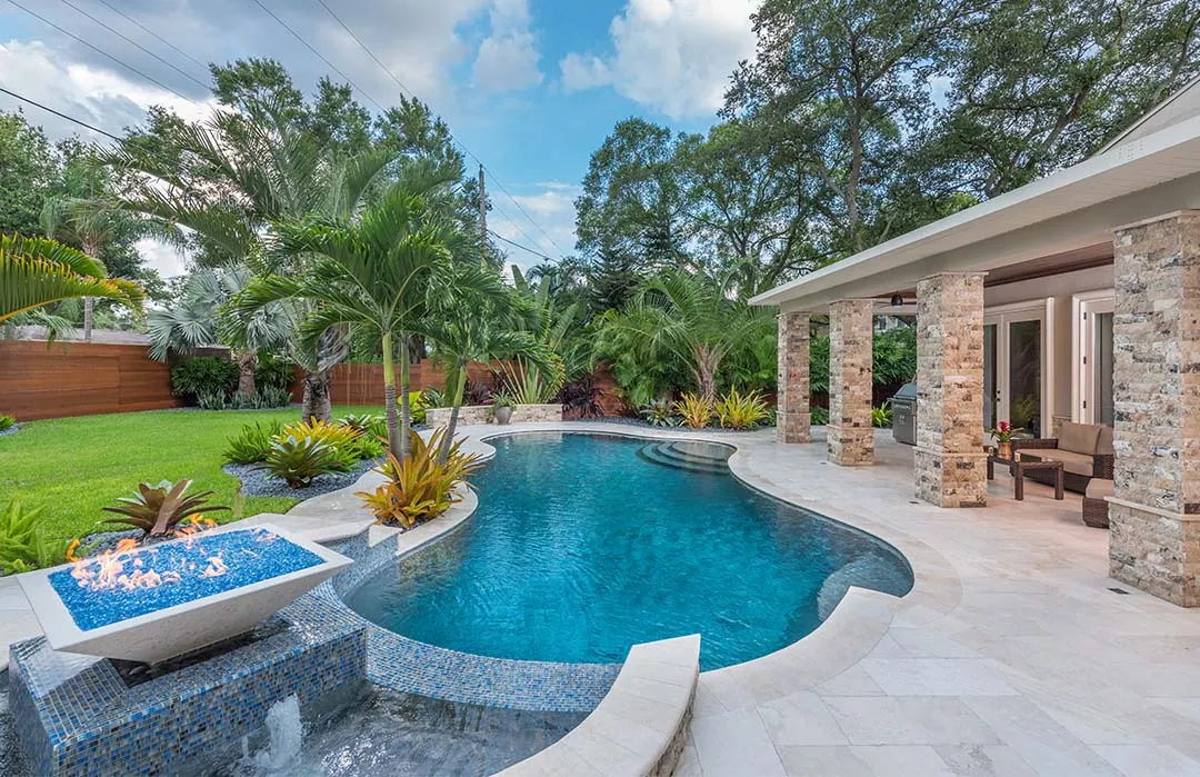 Luxury backyard pool with curved design, stone patio, and lush tropical landscaping in St Petersburg, FL residential community.