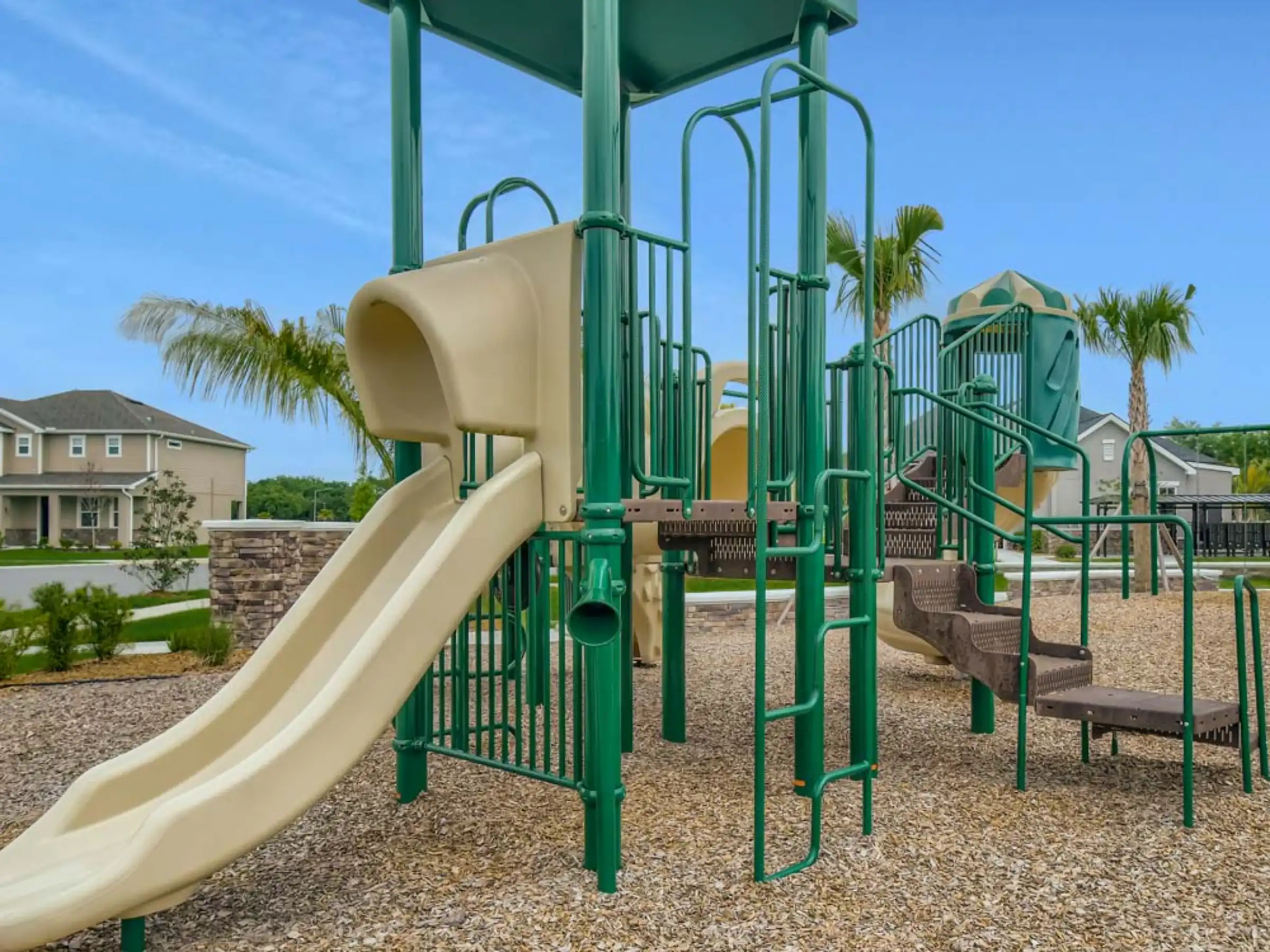 Modern playground with green metal structure and cream spiral slide in residential community near palm trees and homes in St Petersburg, FL.