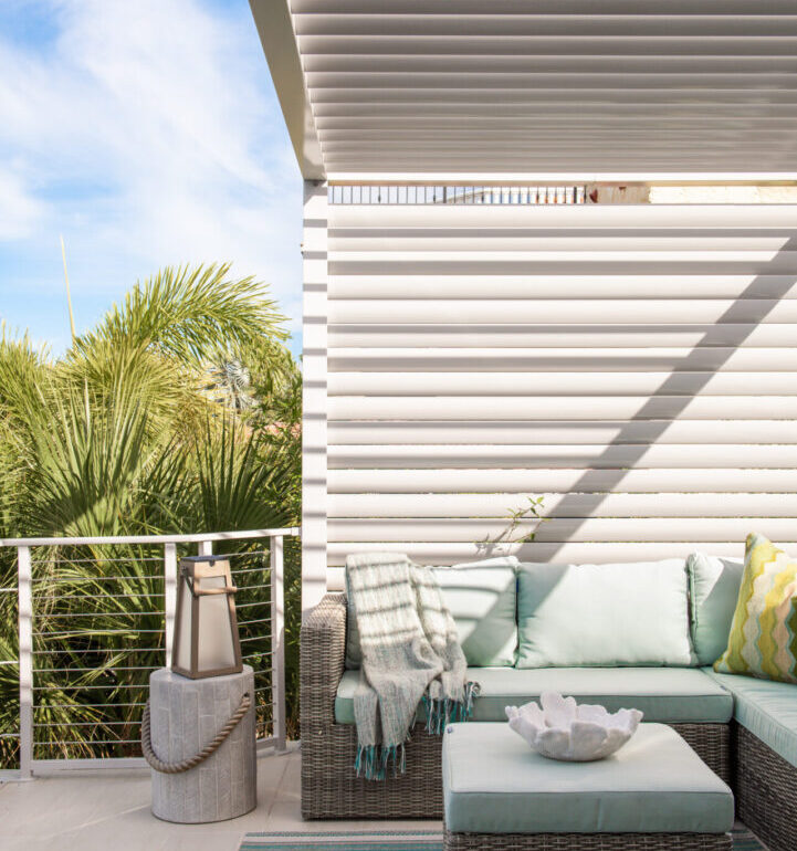 Luxury outdoor lounge with gray wicker sectional, mint cushions, and motorized pergola shade structure overlooking tropical landscaping in St Petersburg.