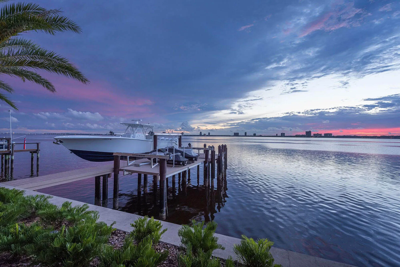 Luxury waterfront dock with moored boat at sunset overlooking St Petersburg Bay with distant skyline and palm trees.