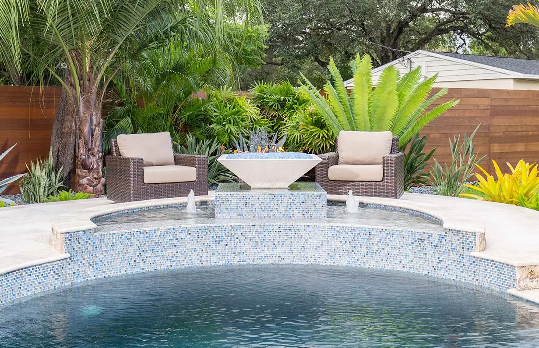 Luxury pool with blue mosaic tile surround and central fire feature, surrounded by tropical landscaping and modern outdoor seating in St Petersburg.