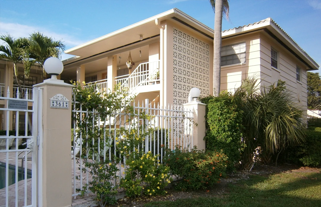 Beige residential home with white railings and decorative lattice screening, featuring tropical landscaping and palm trees in St Petersburg, Florida.