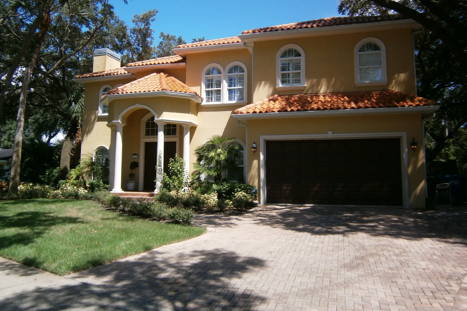 Two-story Mediterranean home with cream stucco exterior, terracotta tile roof, arched entryway, and circular driveway in St Petersburg FL luxury residential community.