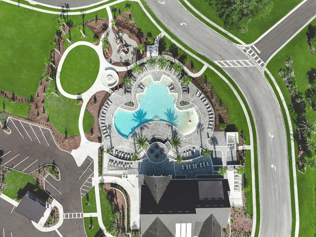 Aerial view of luxury pool complex with turquoise lagoon-style water feature, curved white architectural elements, and manicured landscape design in St Petersburg residential community.