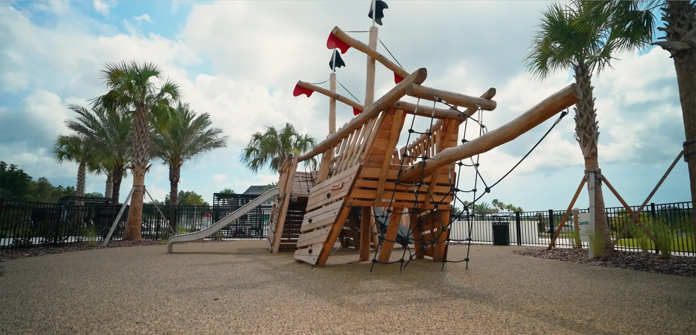 Wooden pirate ship-themed playground with slide, climbing features, and red flags surrounded by palm trees in St Petersburg FL residential community.