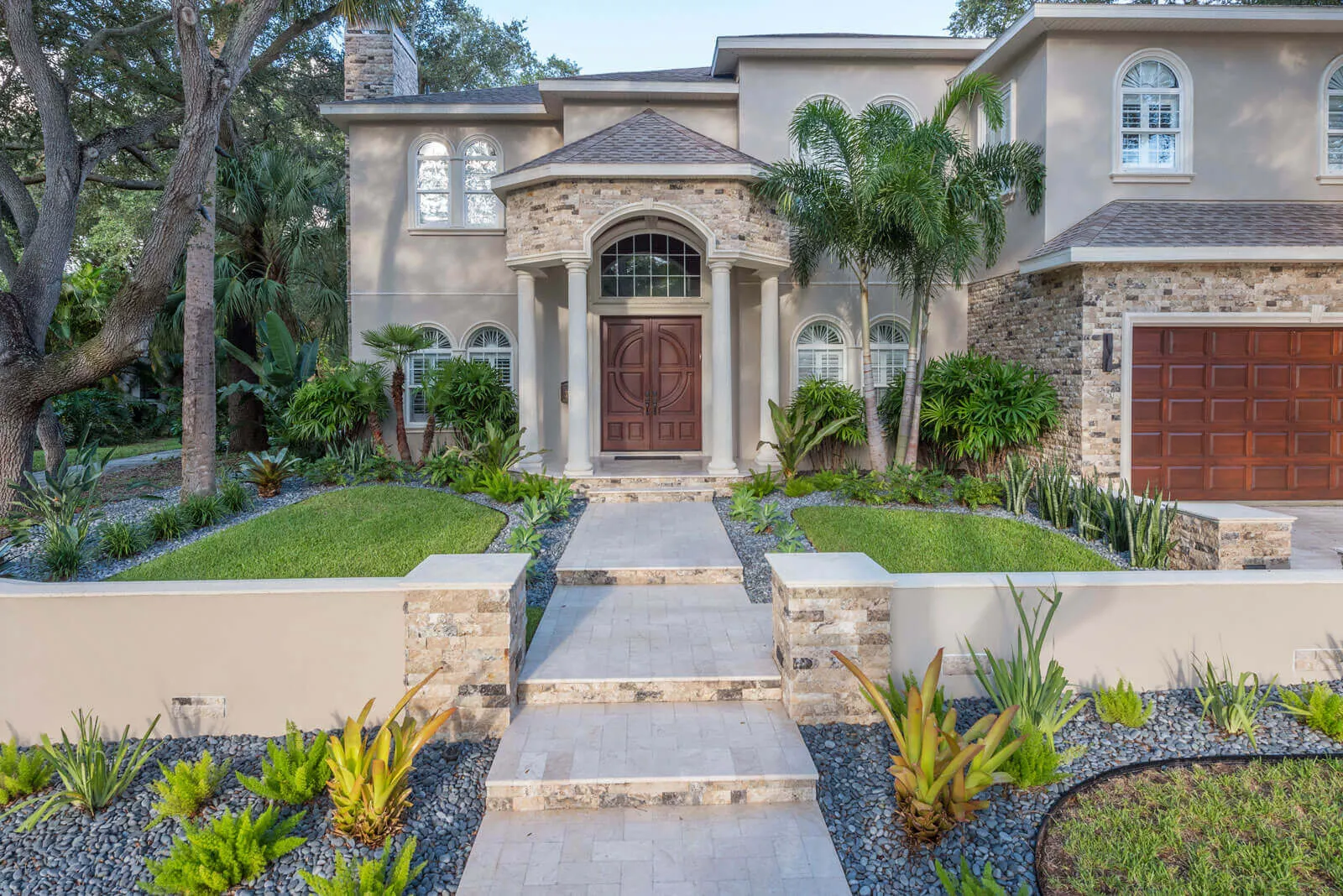 Luxury home exterior featuring stone portico entry with classical columns, tropical plants, and manicured lawn in St Petersburg residential community.