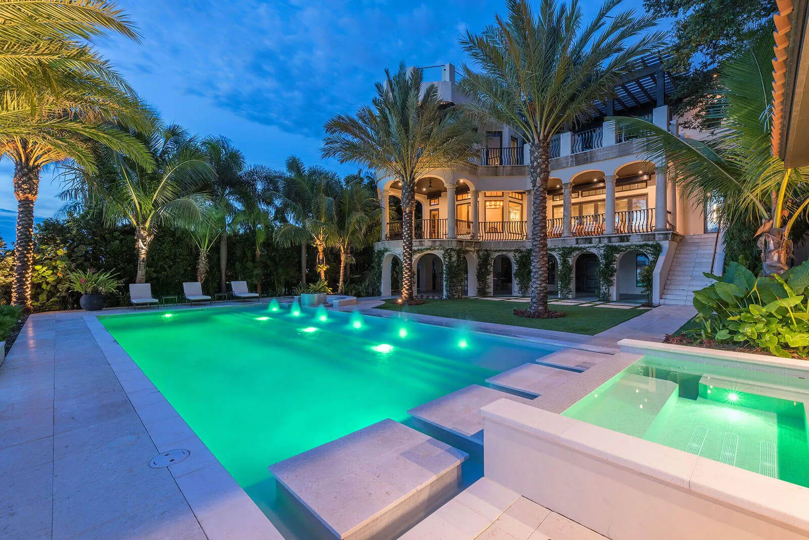 Luxury residential property in St Petersburg FL featuring illuminated pool with green lighting, classical architecture, palm trees, and manicured landscape design.