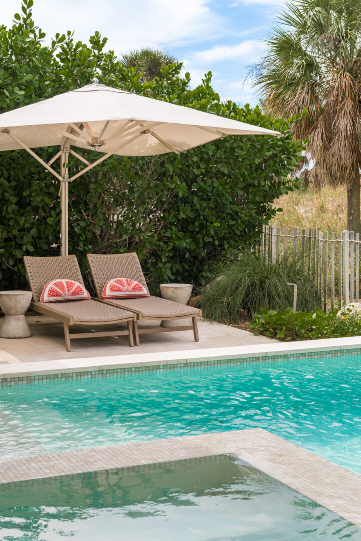 Luxury pool deck with two chaise lounges beneath a large cream umbrella, tropical landscaping, and turquoise swimming pool in St Petersburg residential community.