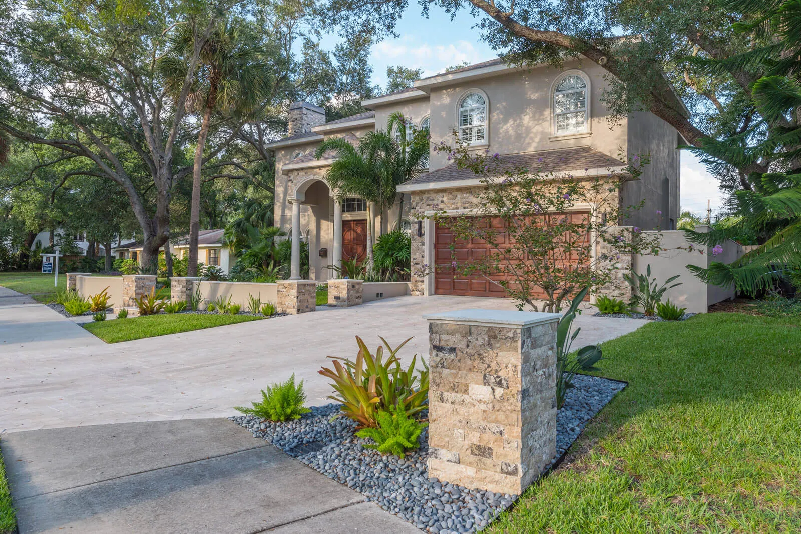Luxury two-story stone colonial home with arched entry, red garage doors, and mature trees in St Petersburg, FL residential community.