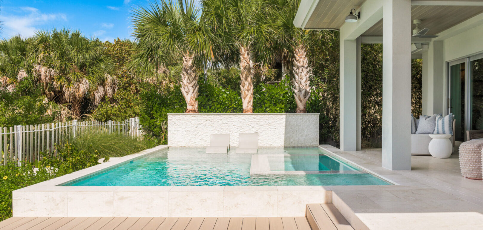Contemporary pool with lounge chairs, white stone surround, and tall palm trees in luxury St Petersburg residential landscape design.