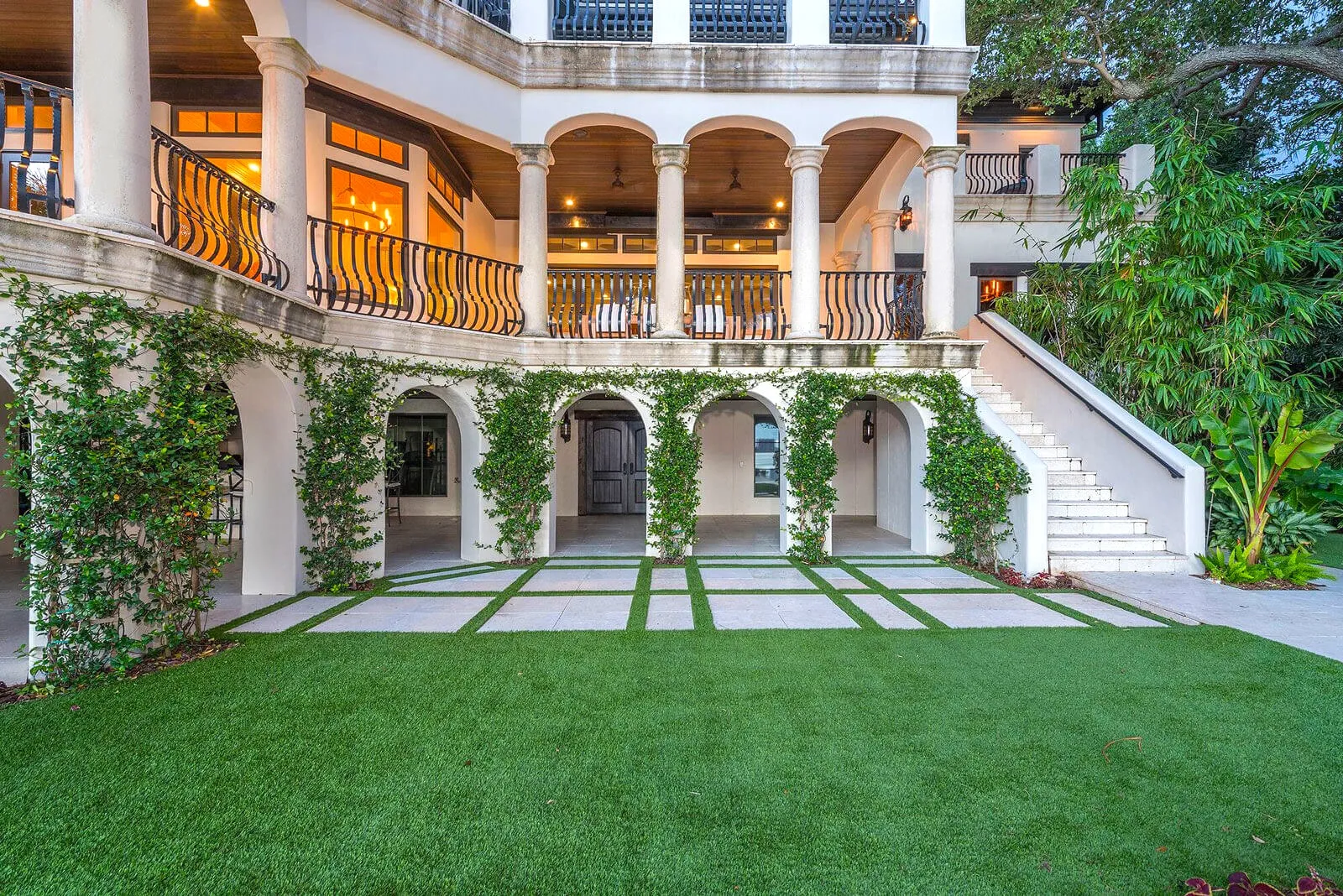 Elegant white stucco building with arched colonnades covered in climbing ivy, manicured lawn, and stone pavers in a luxury residential courtyard design.