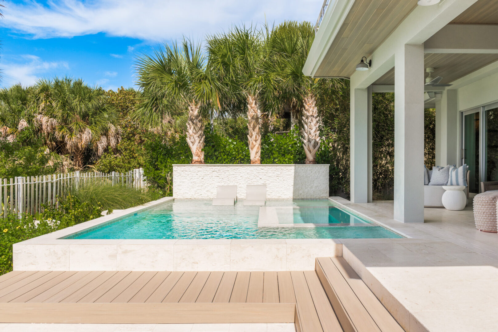 Contemporary pool with lounge chairs, white stone surround, and tall palm trees in luxury St Petersburg residential landscape design.