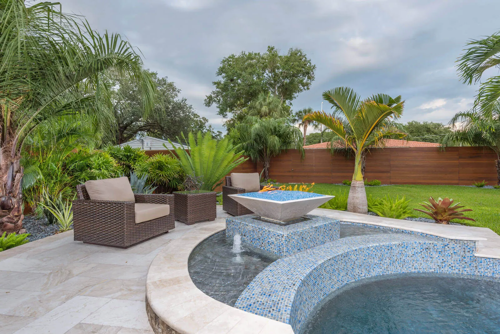 Elegant backyard pool area with blue mosaic tile work, woven lounge seating, and tropical landscape design in St Petersburg, FL.