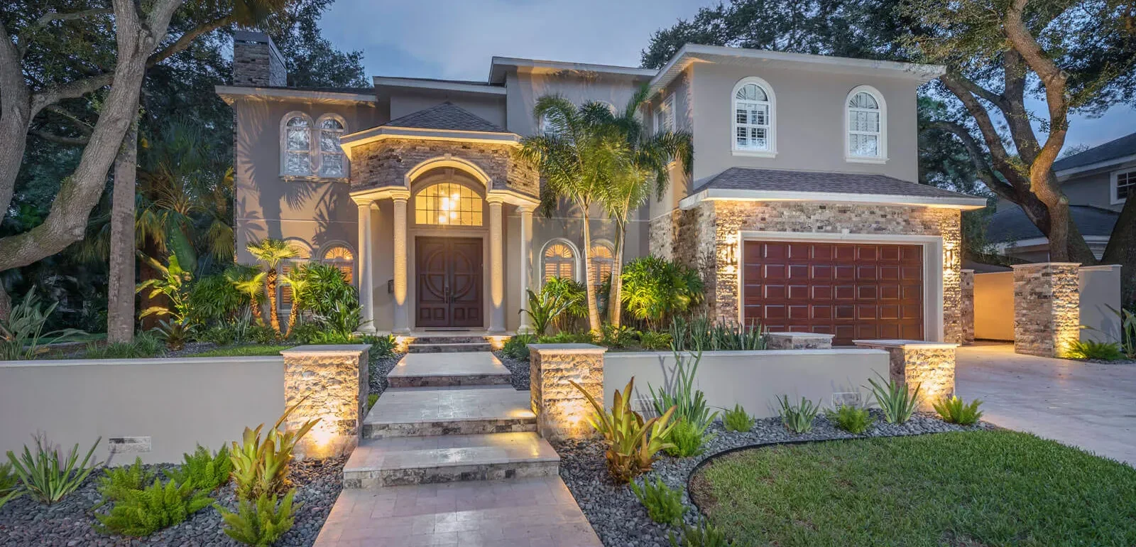 Contemporary home with stone accents and uplighting at dusk in St Petersburg FL, featuring luxury landscape design and architectural details.