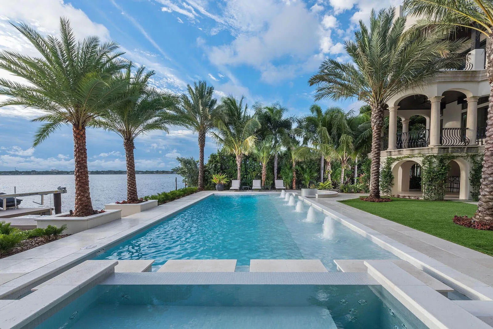 Luxury waterfront home with turquoise pool, manicured lawn, palm trees, and boat dock on St Petersburg bay with classical architecture.
