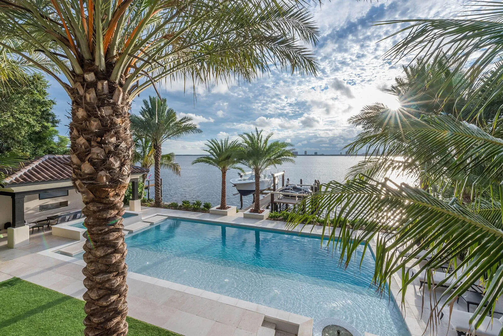 Luxury pool overlooking Biscayne Bay with palm trees, boat dock, and manicured lawn in St Petersburg residential community.