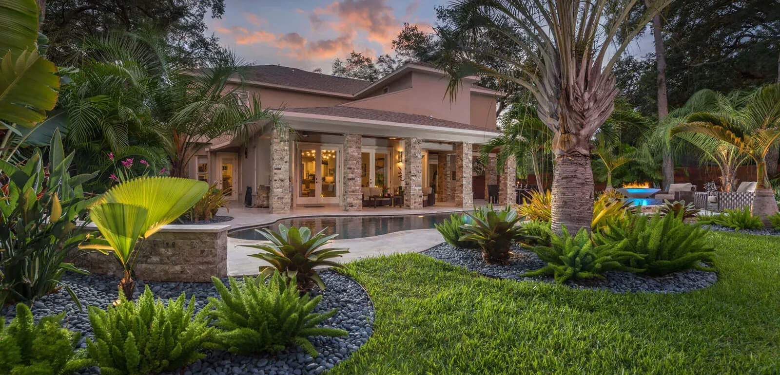 Modern residential home with stone accents surrounded by palm trees and manicured lawn at dusk in St Petersburg, FL.