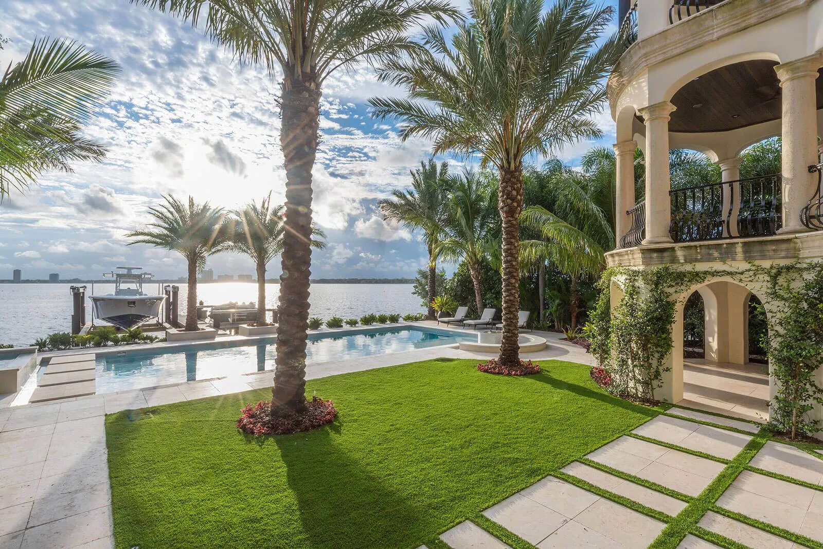 Luxury waterfront home with swimming pool, palm-lined landscape, and columned portico overlooking bay in St Petersburg, FL residential community.