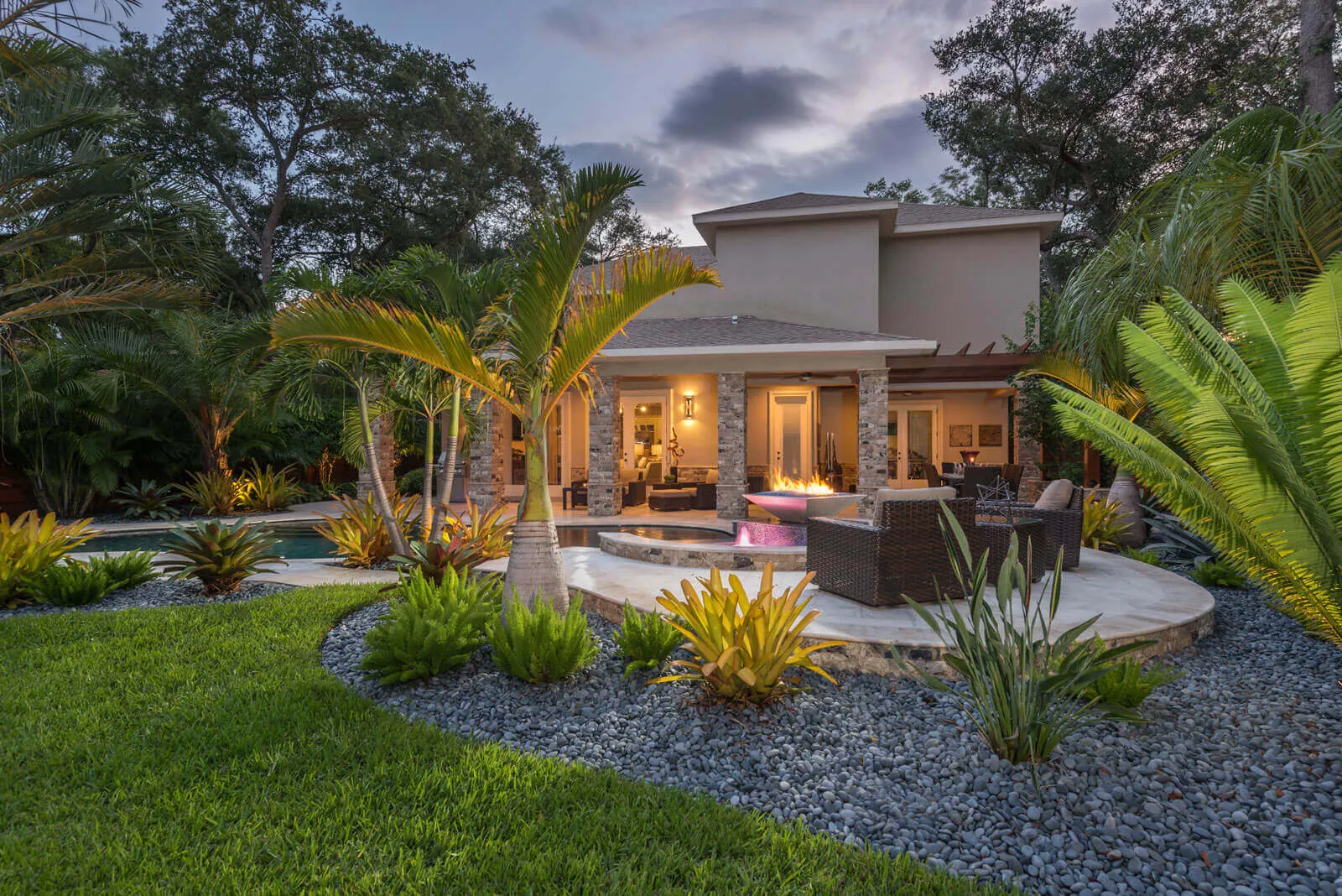 Modern home with stone fireplace, illuminated patio, pool, and tropical landscape design in St Petersburg residential community.